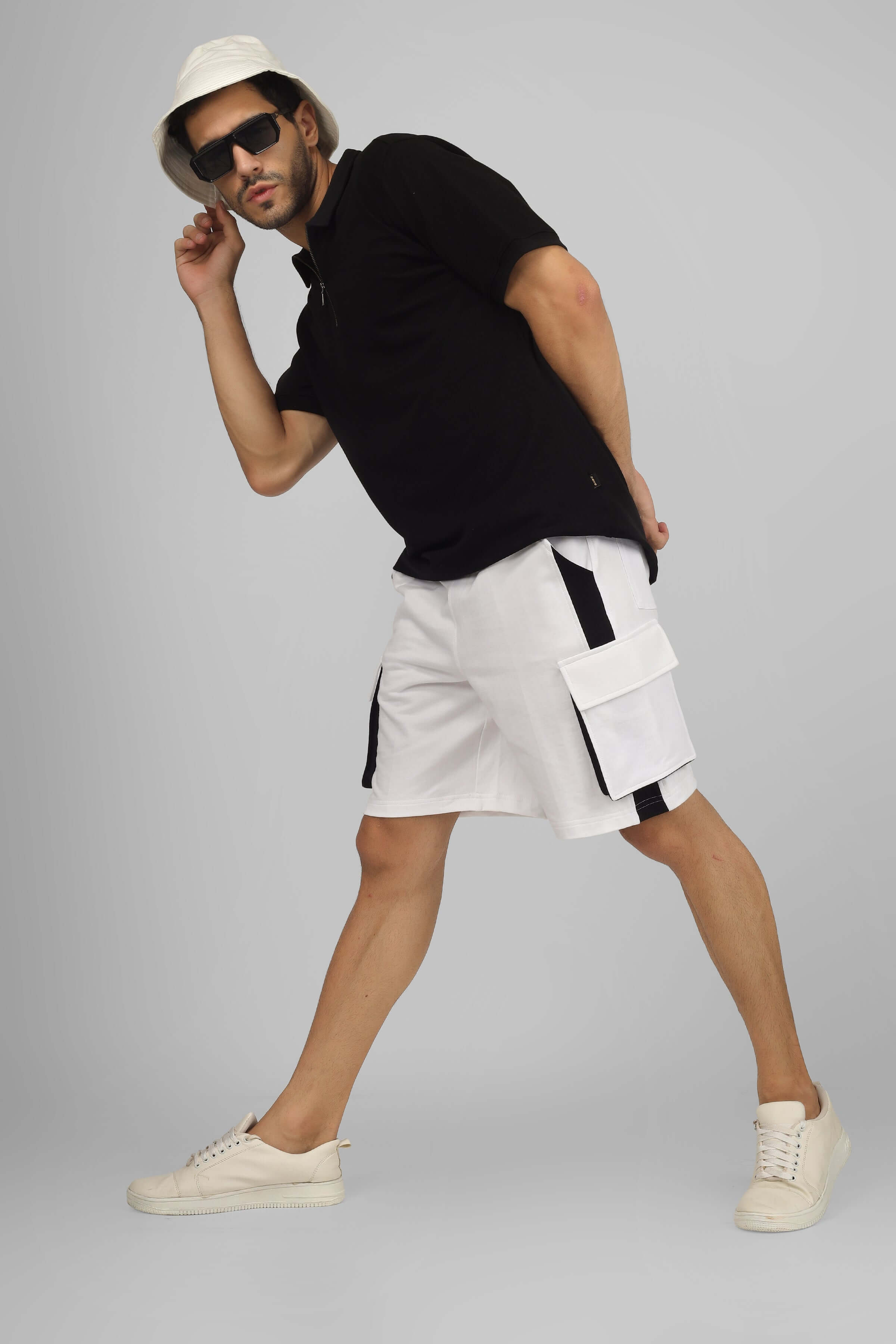 Model wearing CONTRA Regular Fit Cargo Shorts in white and black, paired with a black polo, white sneakers, and a white hat.