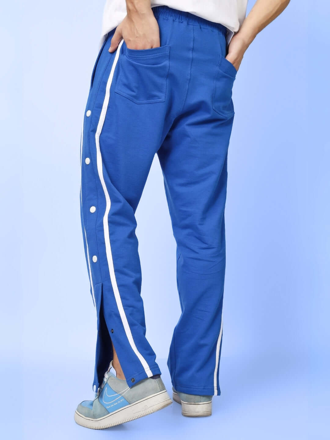Back view of blue contrast panel joggers with side buttons and white stripe detail, worn by a person standing casually.