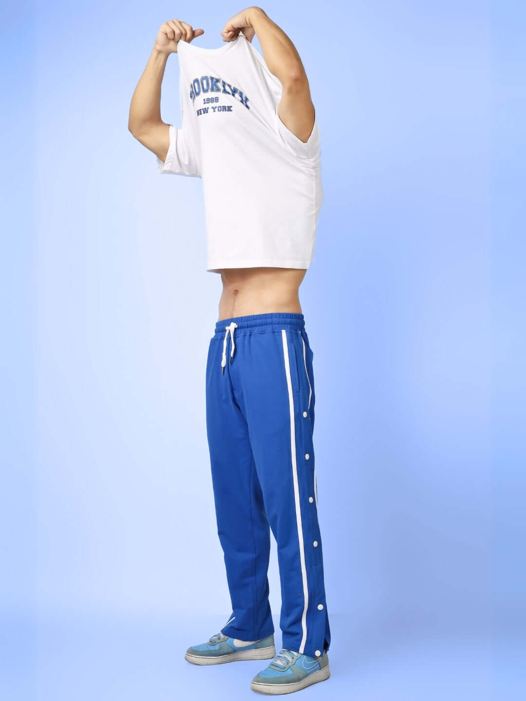 Man wearing blue contrast panel joggers from DUDS, featuring side stripes and buttons, on a light blue background.