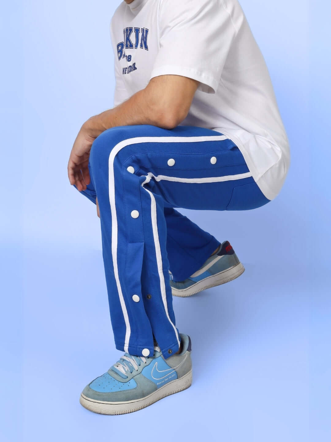 Man wearing blue contrast panel joggers with button details, paired with white sneakers.