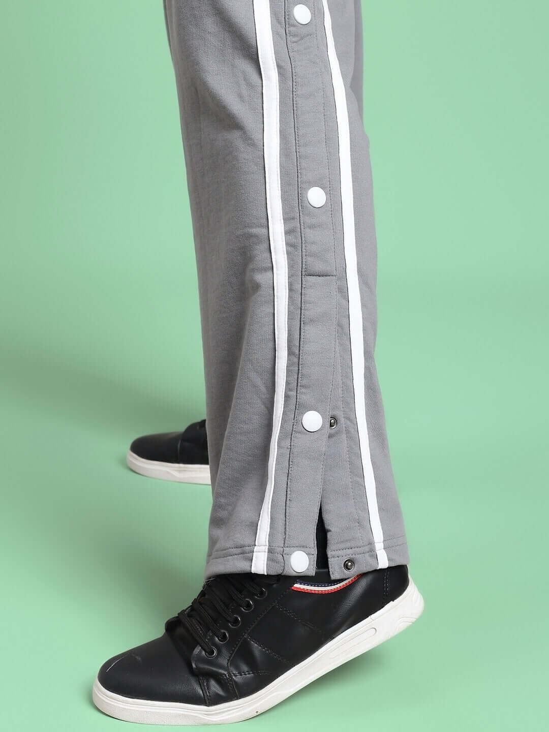 Side view of CONTRAST PANEL COTTON TERRY JOGGER GREY showing detail of the contrast panel and snap buttons, paired with black sneakers.