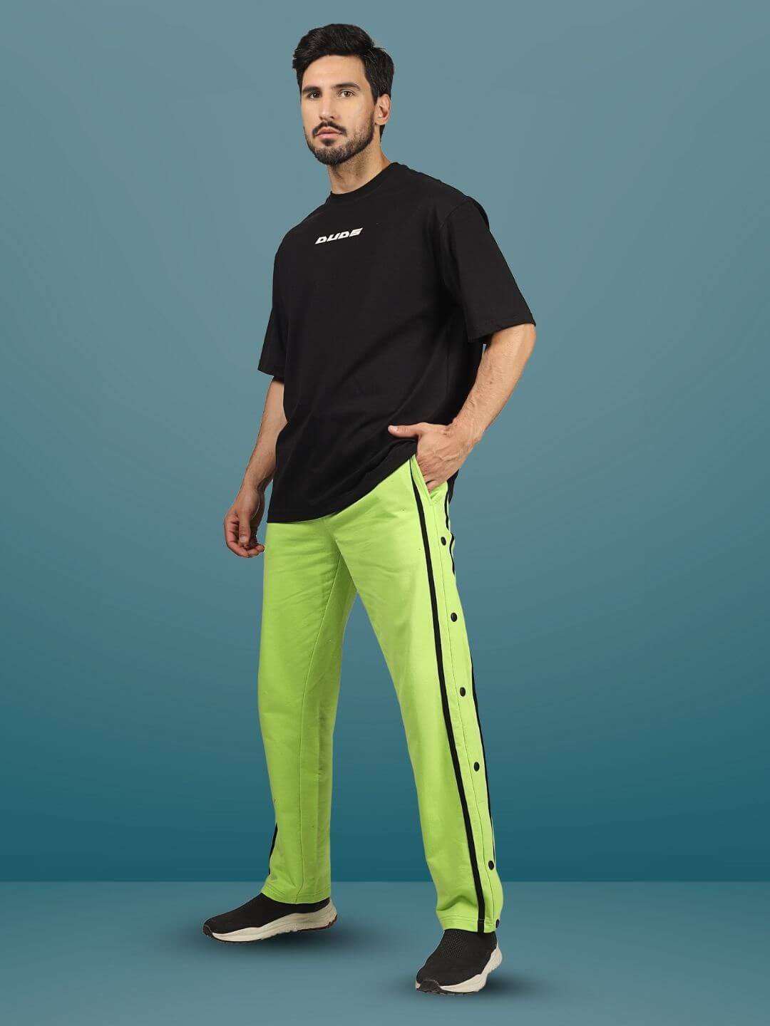 Model wearing contrast panel joggers in neon green with black side stripes and button details, paired with a black oversized T-shirt.