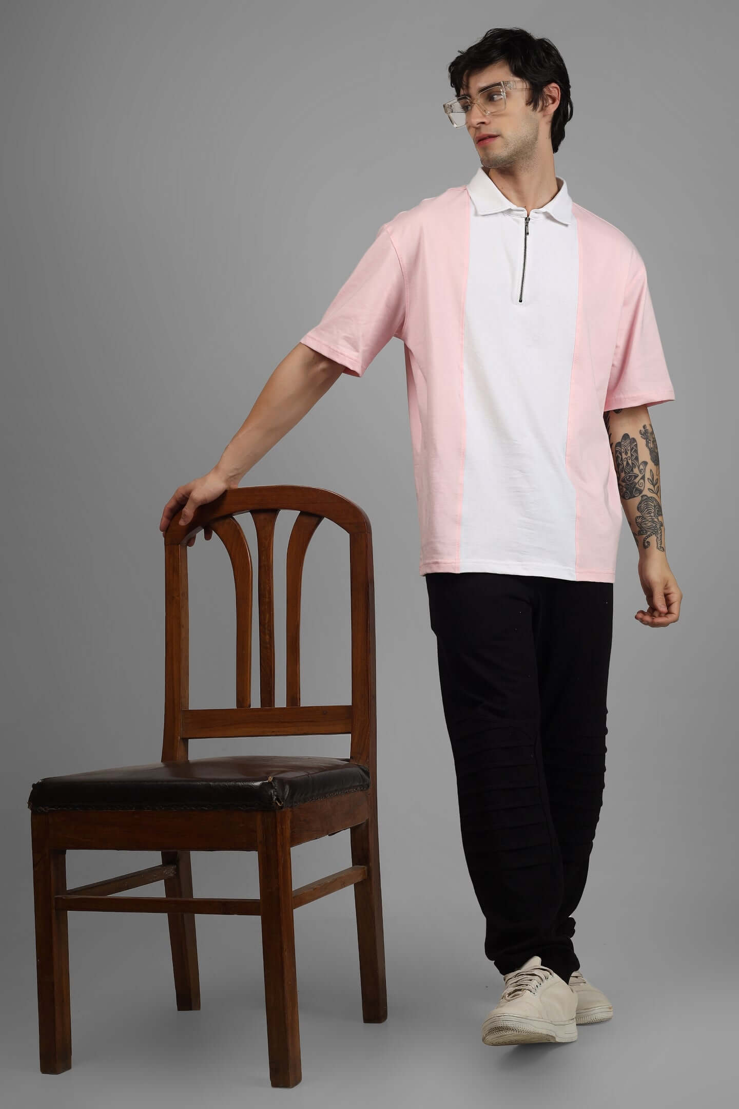 Model wearing blush pink-white contrast polo oversized zipper T-shirt, paired with black pants, standing beside a wooden chair.