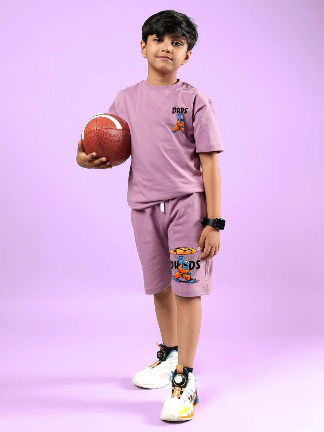 Child wearing COOKIE MONSTER PRINTED CO-ORD FOR BOYS & GIRLS PLUM PURPLE holding a basketball on a purple background.