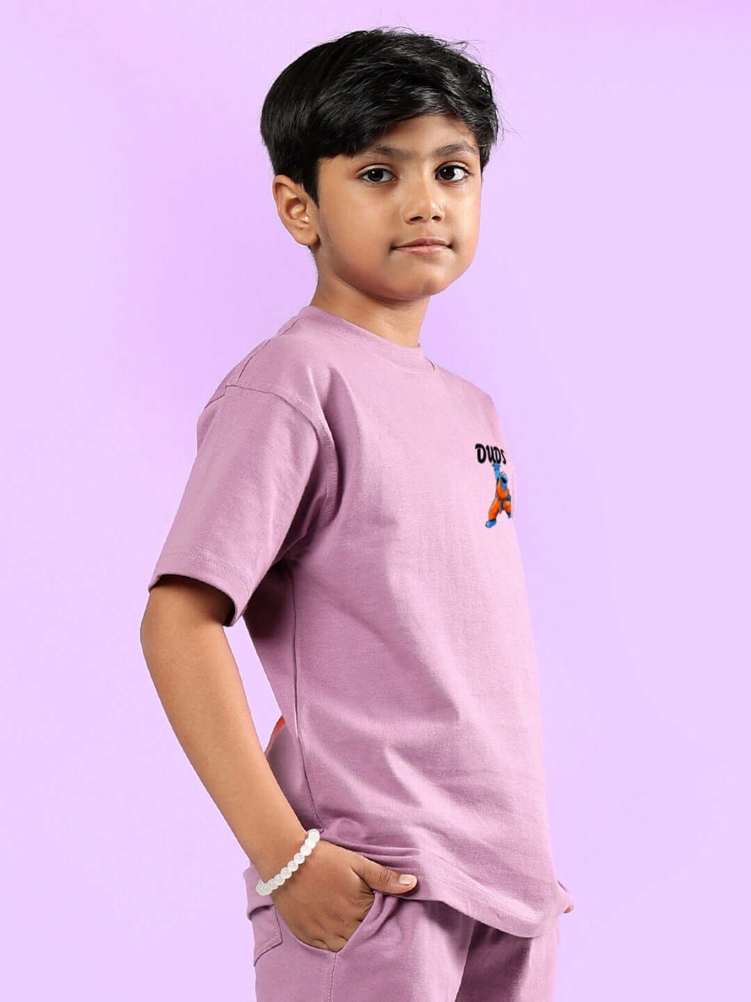 Child wearing COOKIE MONSTER PRINTED T-SHIRT FOR BOYS & GIRLS PLUM PURPLE, standing against a purple background.