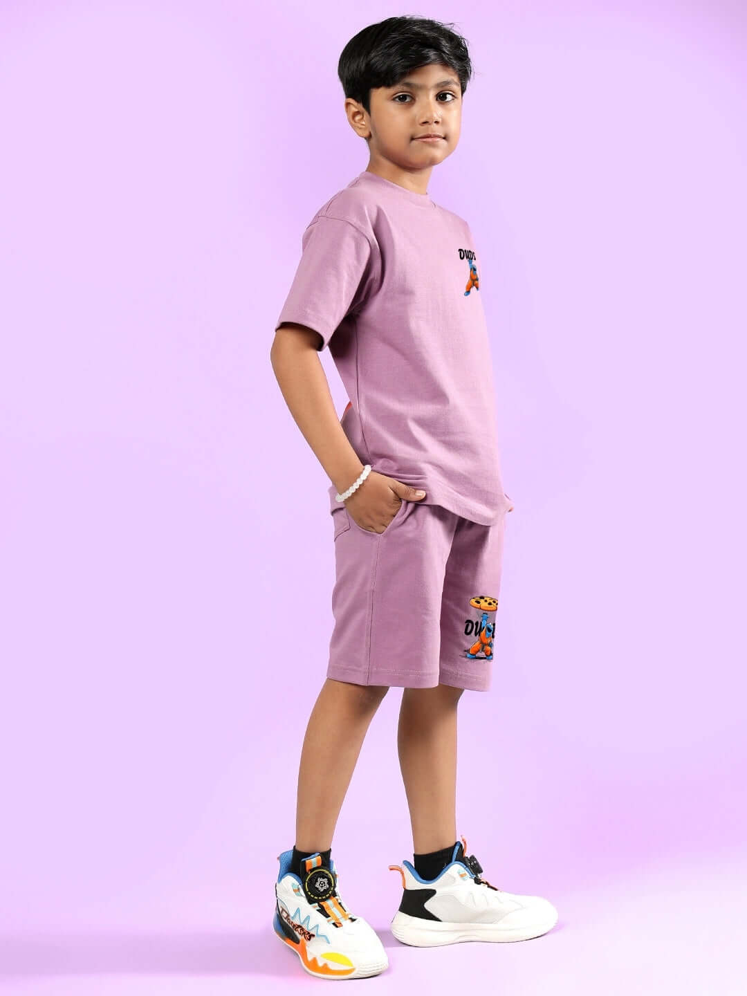 Alt Tag: Young boy wearing COOKIE MONSTER PRINTED CO-ORD FOR BOYS & GIRLS PLUM PURPLE outfit standing against a matching purple background.