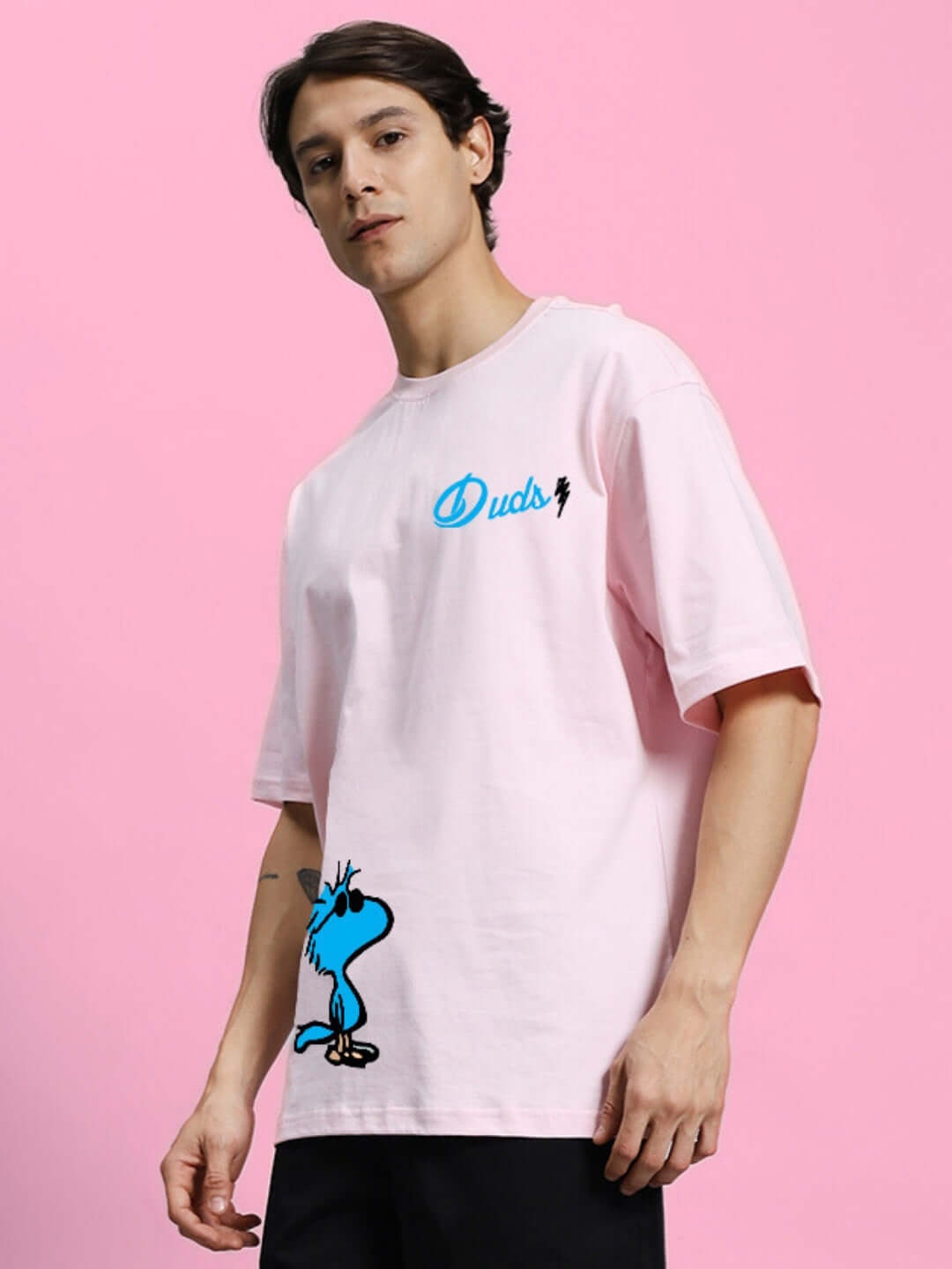 Model wearing COOL PALS PRINTED OVERSIZED T-SHIRT PINK with cartoon character graphic on pink background.