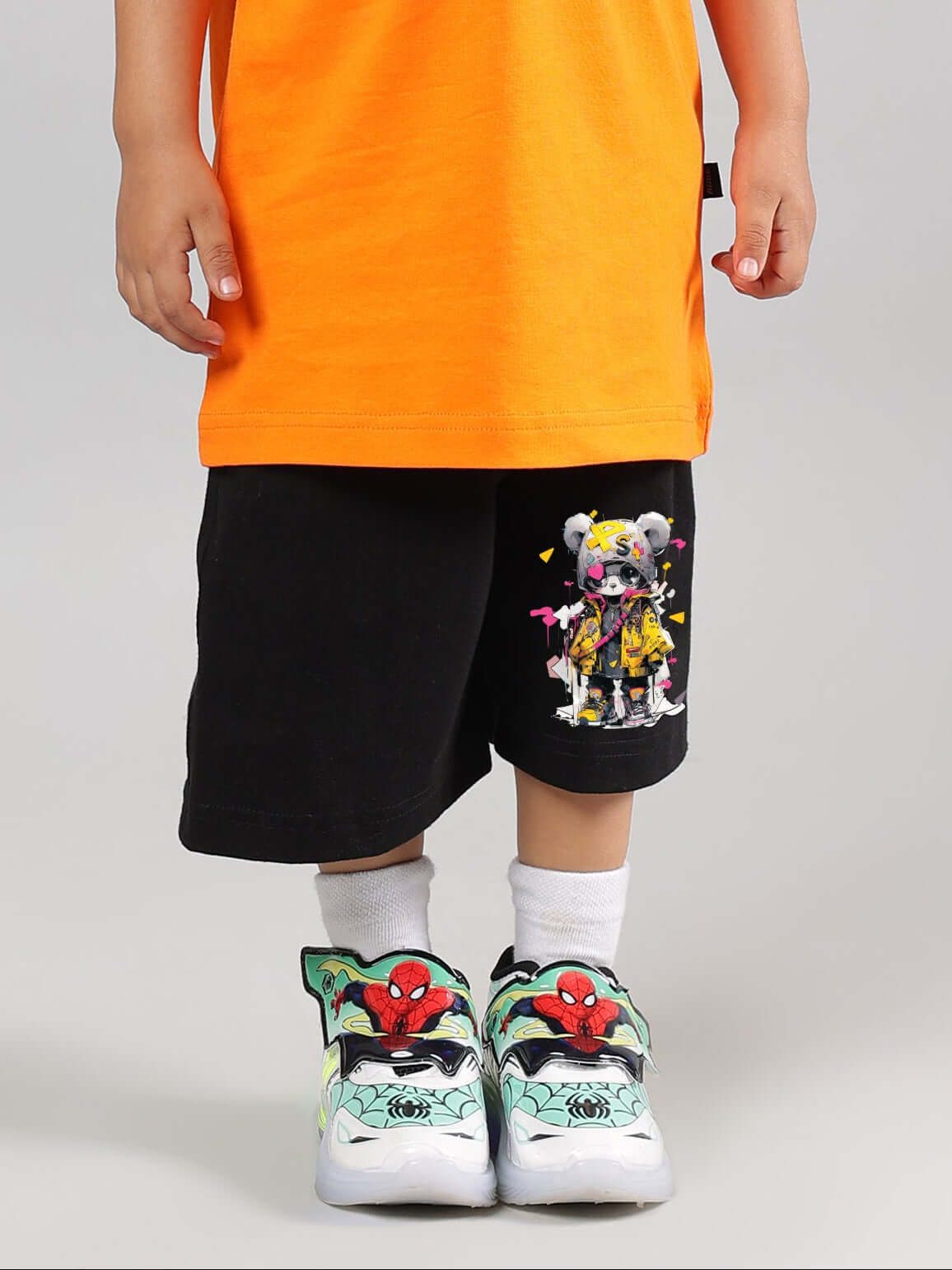 Child wearing cool teddy print black shorts by DUDS, paired with colorful sneakers and a bright orange shirt. Ideal for boys and girls.