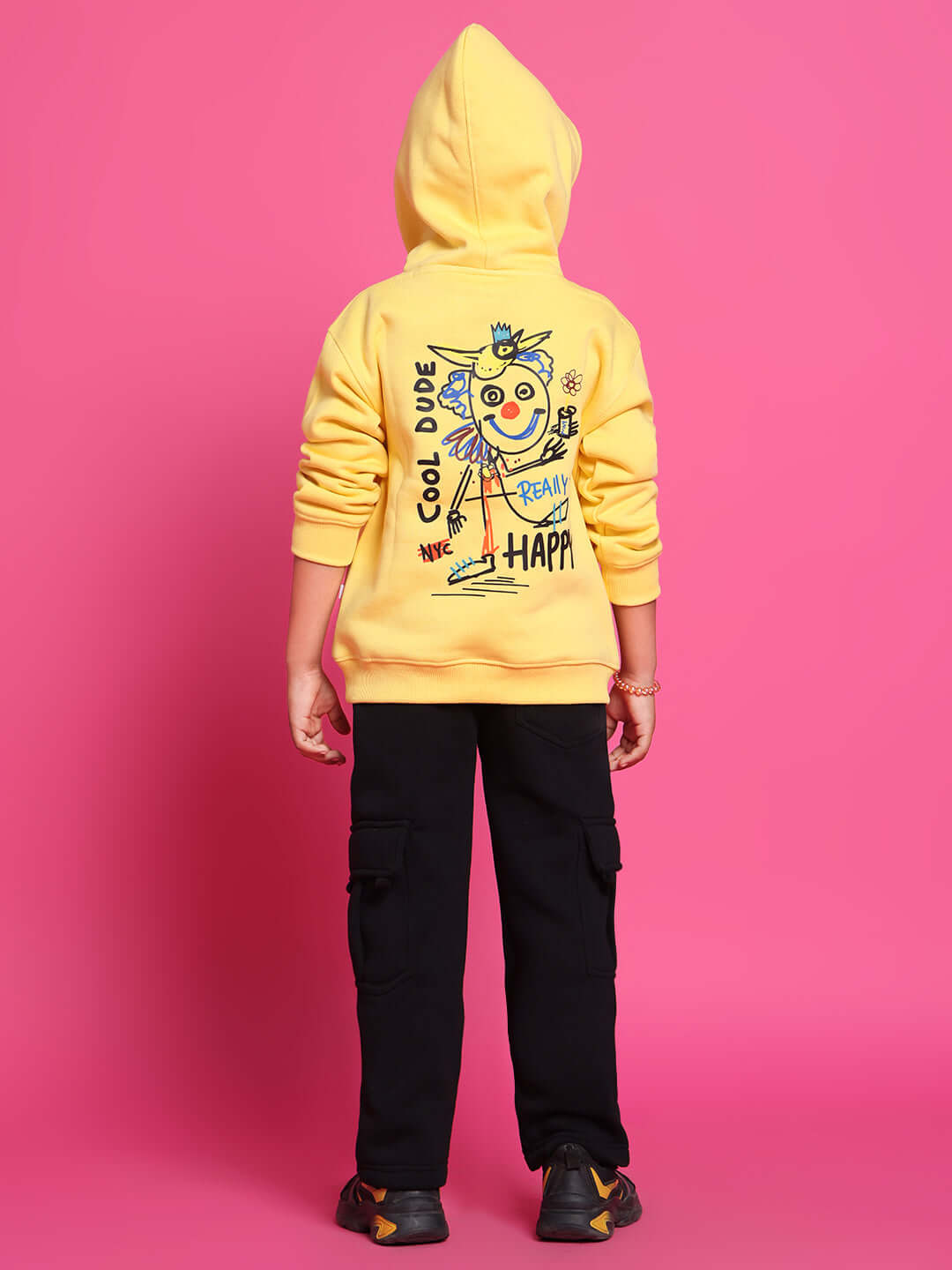 Child wearing COOL DUDE CO-ORD FOR BOYS GIRLS YELLOW hoodie and black pants, pink background.