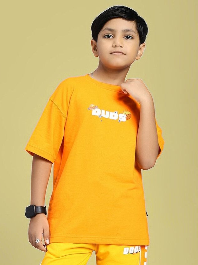 Boy wearing COSMIC CUTE ASTRONAUT T-SHIRT FOR BOYS AND GIRLS ORANGE with astronaut graphic on vibrant orange backdrop.