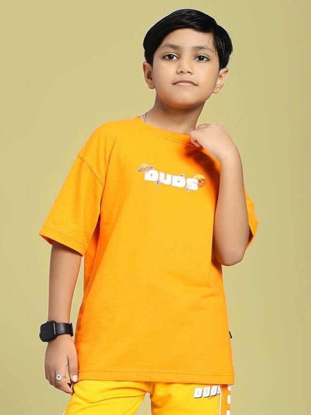 Boy wearing COSMIC CUTE ASTRONAUT T-SHIRT FOR BOYS AND GIRLS ORANGE with astronaut graphic on vibrant orange backdrop.
