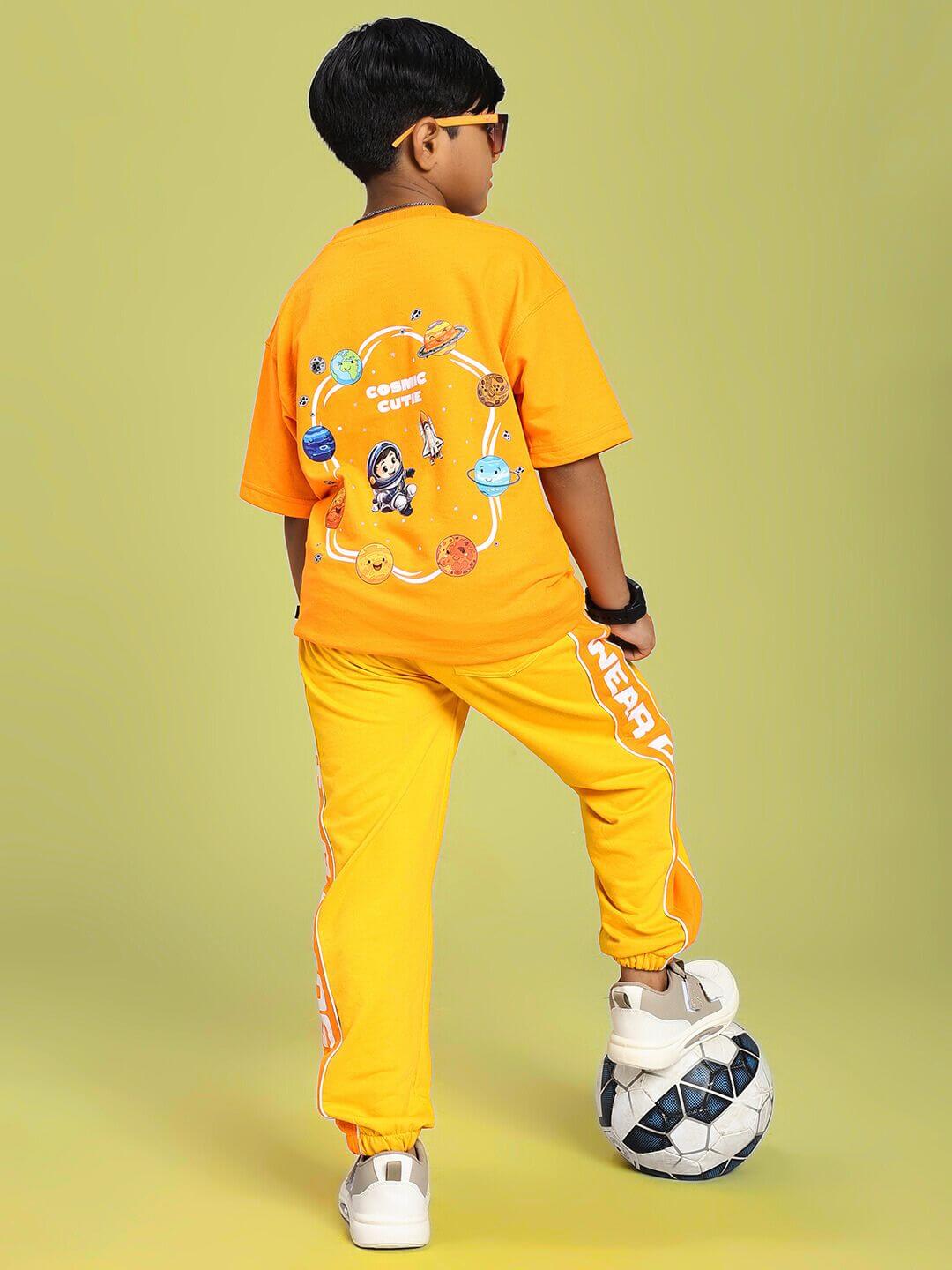 Child wearing COSMIC CUTE ASTRONAUT T-SHIRT FOR BOYS AND GIRLS ORANGE with astronaut graphic, standing with a soccer ball.