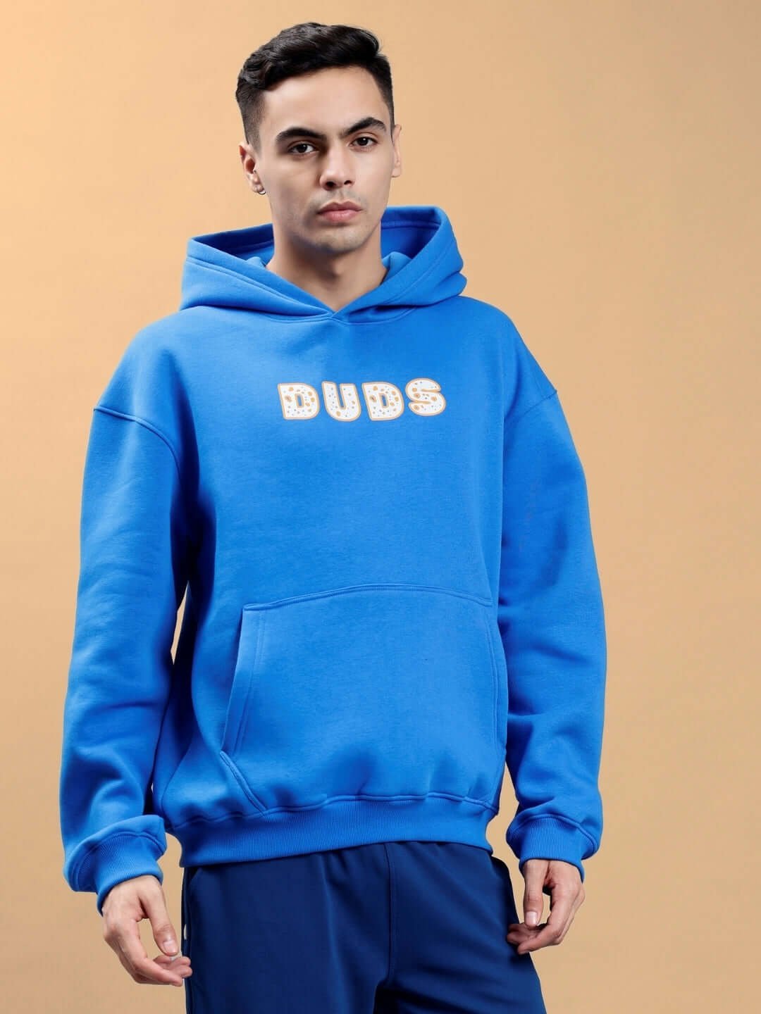 Man wearing a royal blue oversized hoodie with 'DUDS' text, showcasing casual streetwear style.
