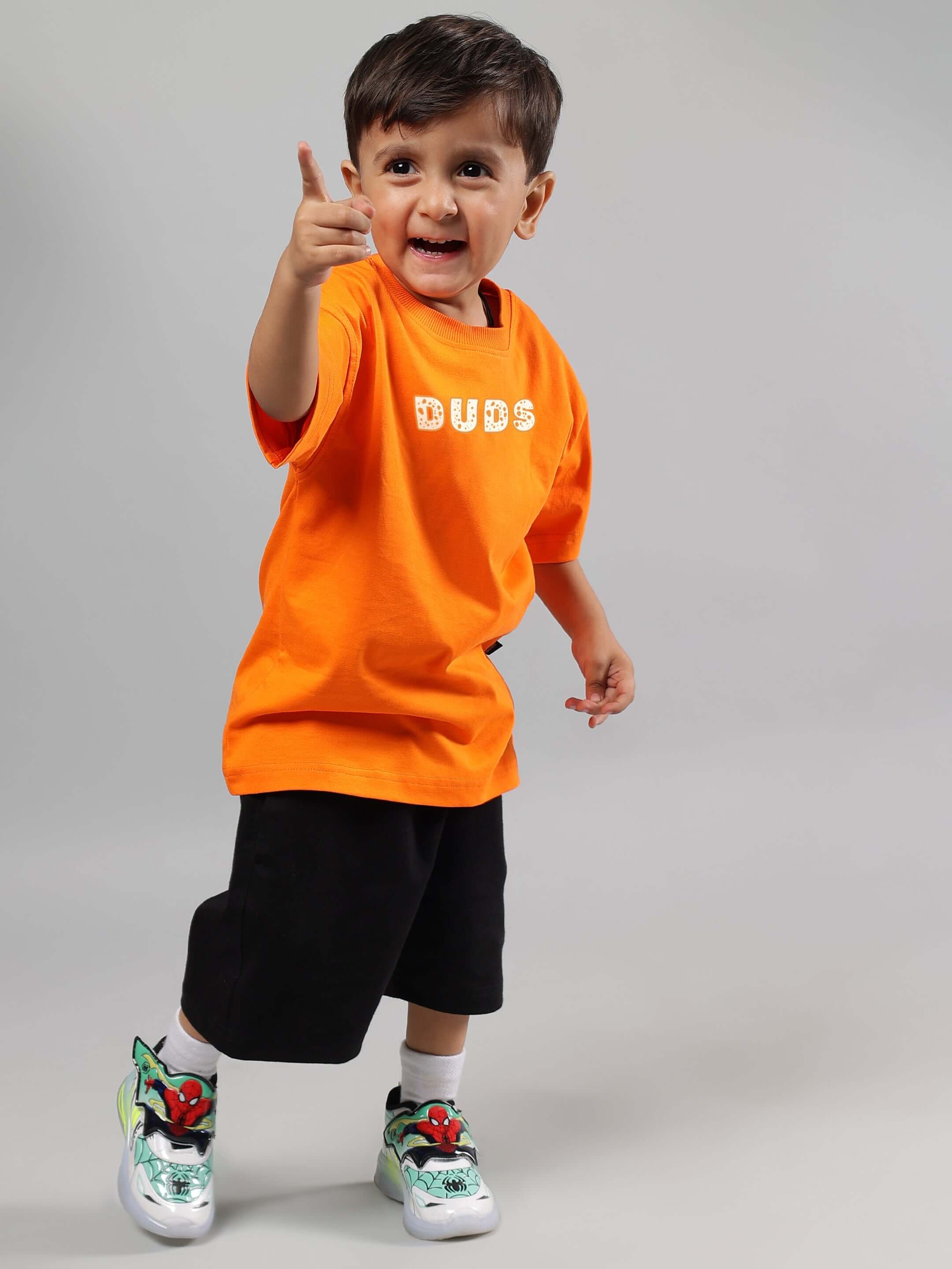 Child wearing COURAGE TOON CO-ORD FOR BOYS GIRLS ORANGE-BLACK set with orange shirt and black shorts, standing and smiling.