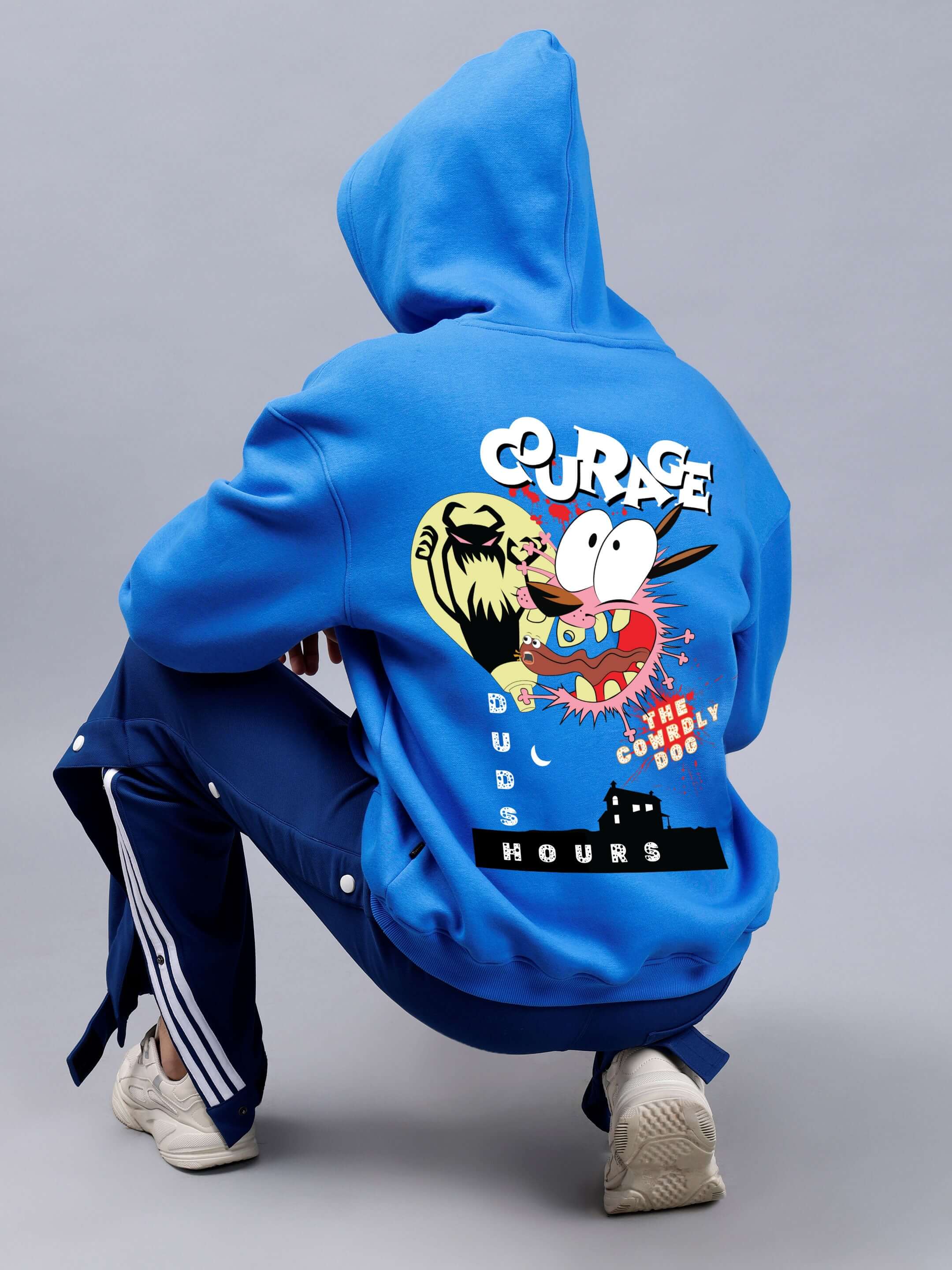 Person wearing a royal blue oversized hoodie with a cartoon graphic and 'COURAGE' text on the back, complemented by sporty navy pants.