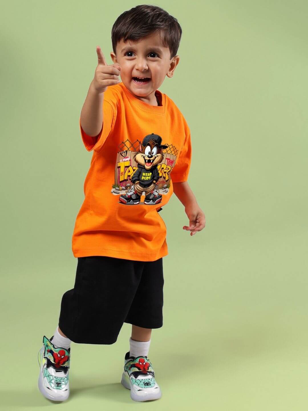 Child wearing Crazy Rapper orange and black co-ord set with cartoon print, smiling and posing against a green background.