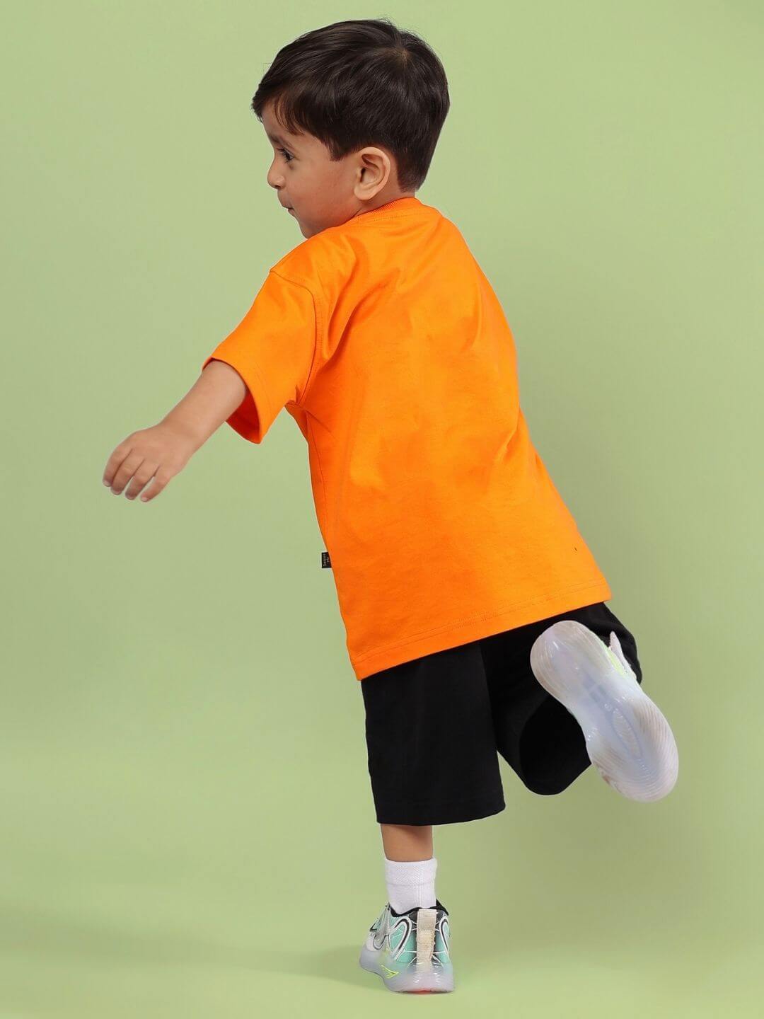 Child wearing CRAZY RAPPER CO-ORD FOR BOYS GIRLS AND ORANGE-BLACK, playful streetwear set, orange top and black shorts, running.