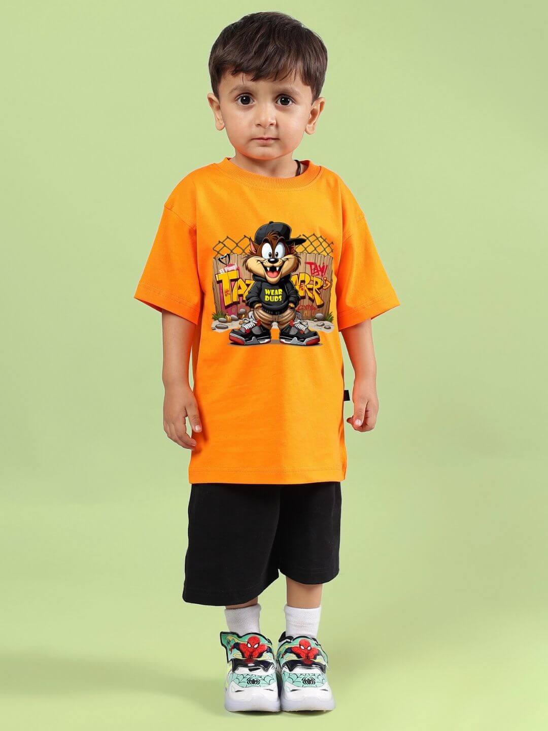 Child wearing CRAZY RAPPER CO-ORD FOR BOYS GIRLS AND ORANGE-BLACK, featuring orange t-shirt with graphic, black shorts, on green background.