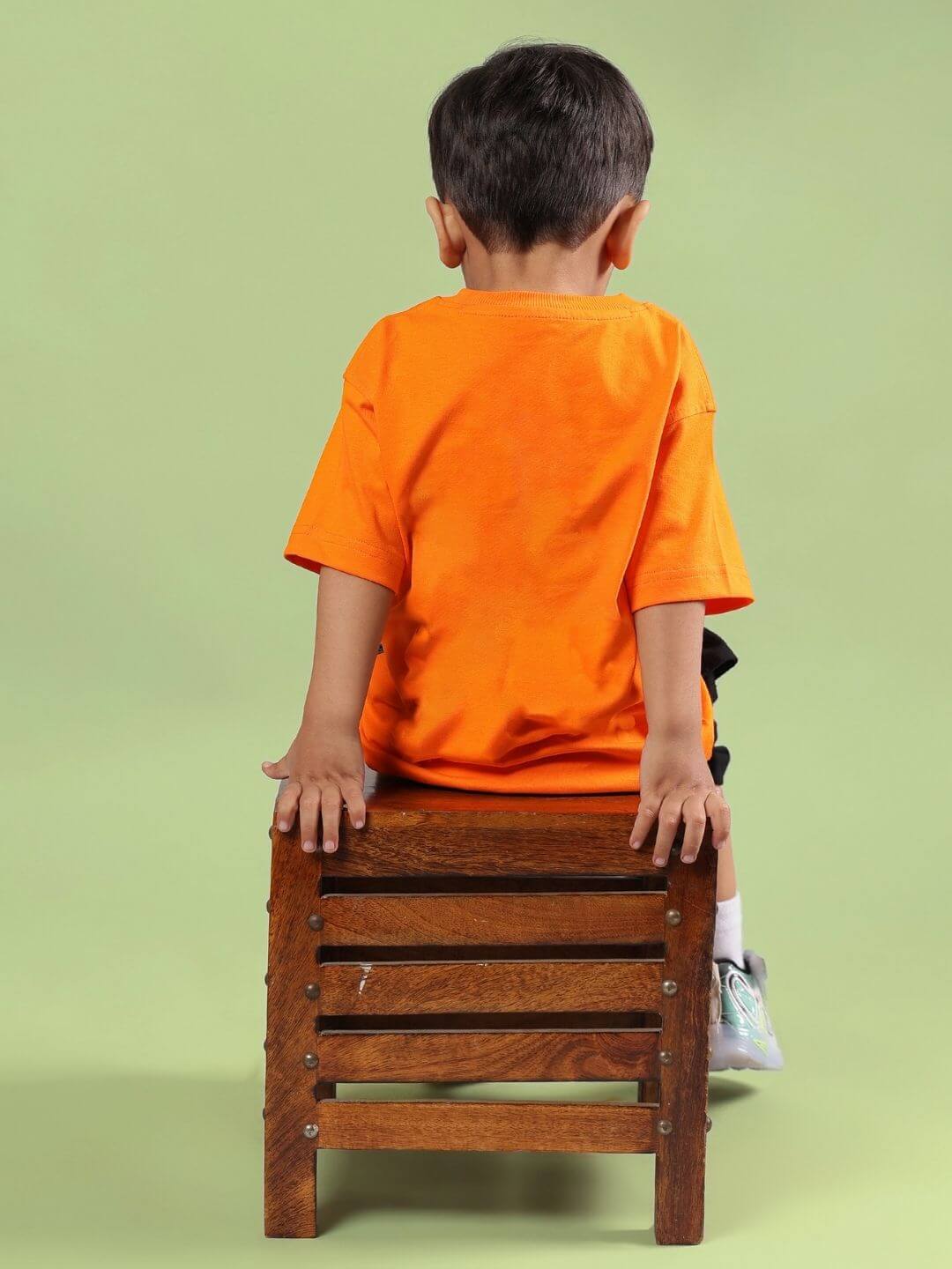 Boy wearing CRAZY RAPPER CO-ORD FOR BOYS GIRLS AND ORANGE-BLACK sitting on a wooden stool, showing the bold orange top from the set.