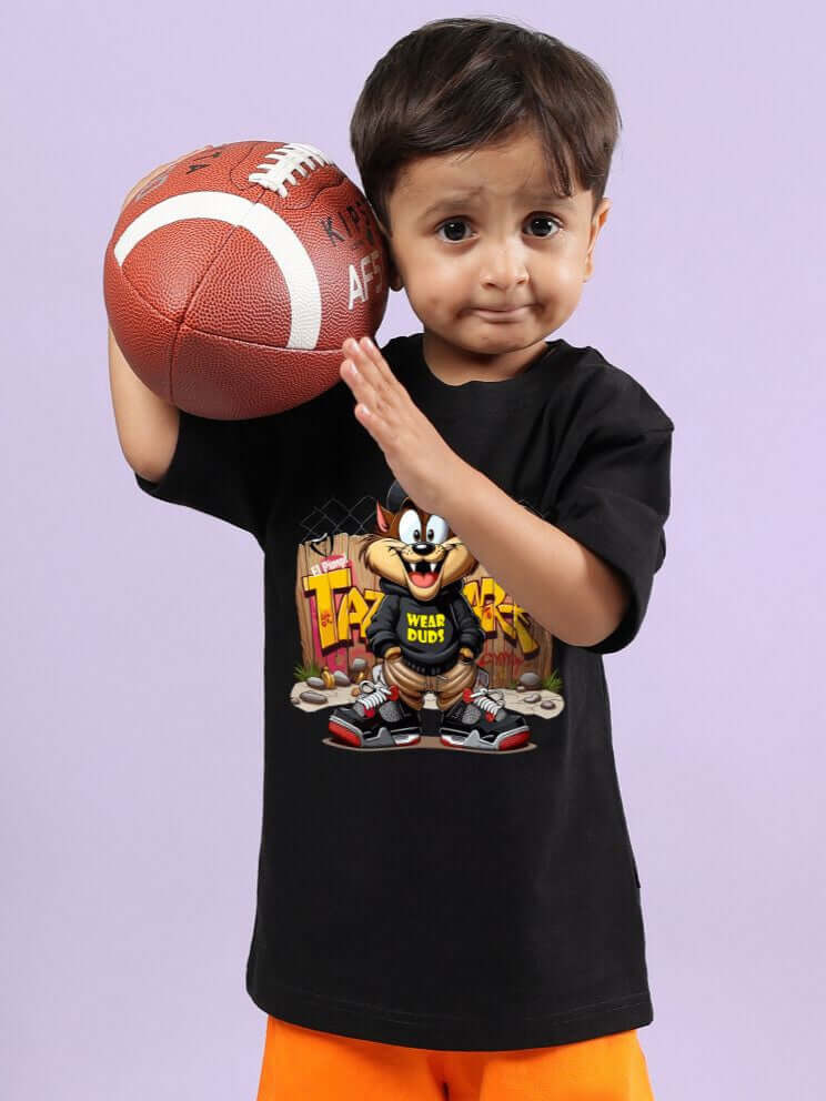 Young boy wearing CRAZY RAPPER T-SHIRT FOR BOYS AND GIRLS BLACK holding a football, showcasing playful streetwear style.