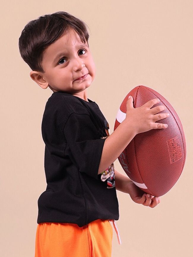 Young child wearing a black t-shirt holding a football, showcasing playful and sporty style.