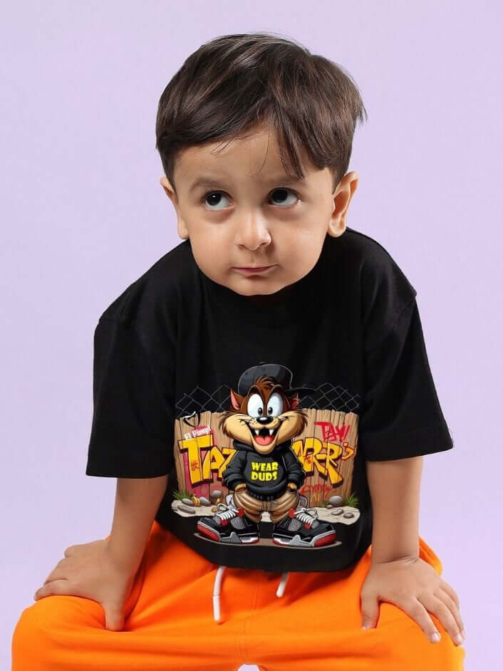 Child wearing CRAZY RAPPER T-SHIRT FOR BOYS AND GIRLS BLACK, featuring cartoon print, sitting with hands on knees, showcasing trendy kidswear.