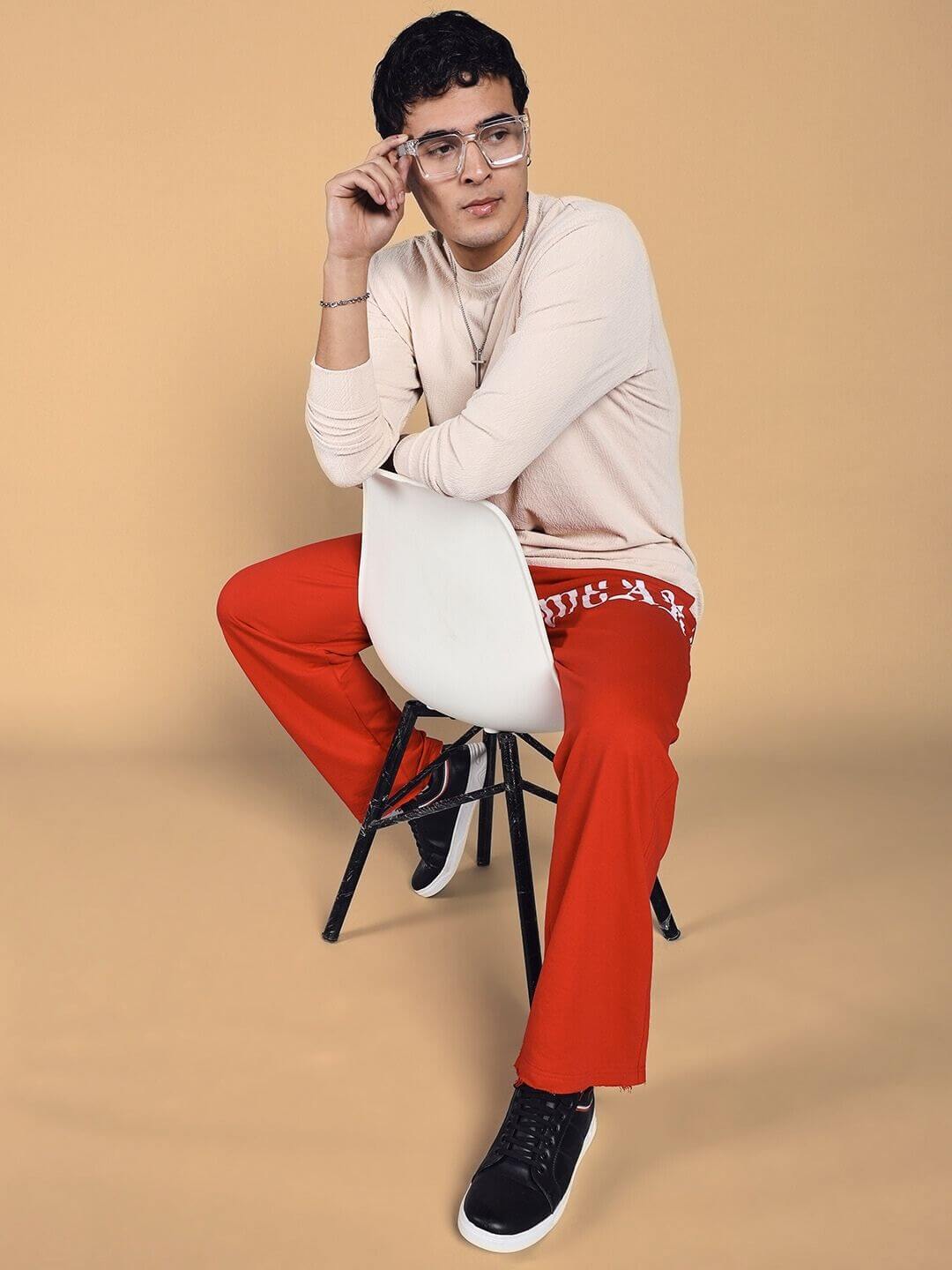 Model wearing CRIMSON RELAXED FIT JOGGER in red, paired with a beige top, seated on a white chair for a stylish look. Custom fit available.