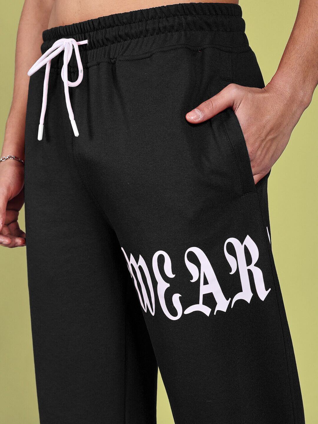 Close-up of black relaxed fit joggers with white drawstring and pocket, featuring bold "WEAR" print.