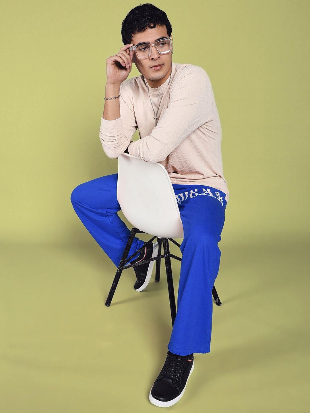 Model wearing crimson relaxed fit jogger in blue, seated stylishly on a chair against a beige background.