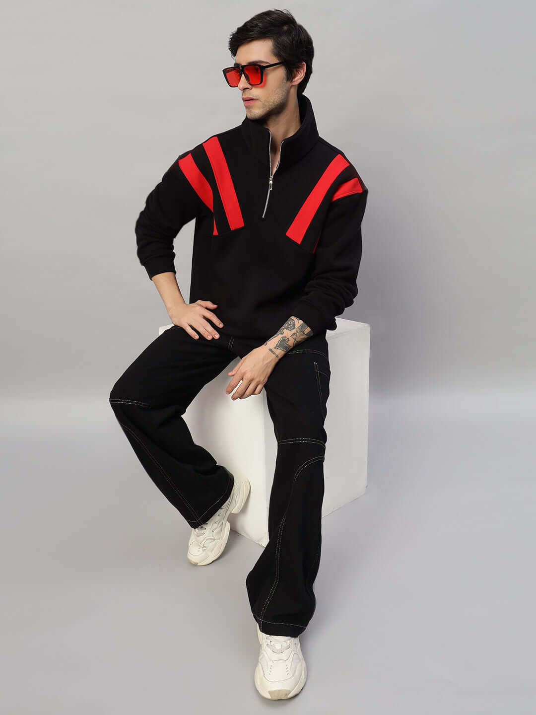 Model wearing CROSSBAR Fleece Colorblock Jacket in black and red, sitting stylishly on a block with red sunglasses.