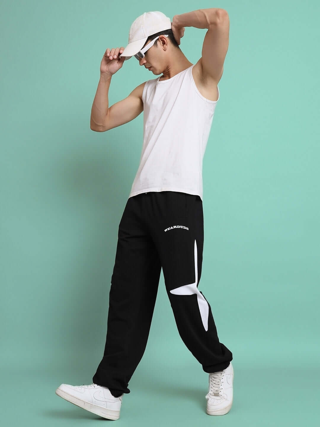 Man wearing CROSSED STAR JOGGER (BLACK) with white tank top and cap, stylish joggers by DUDS with unique design.