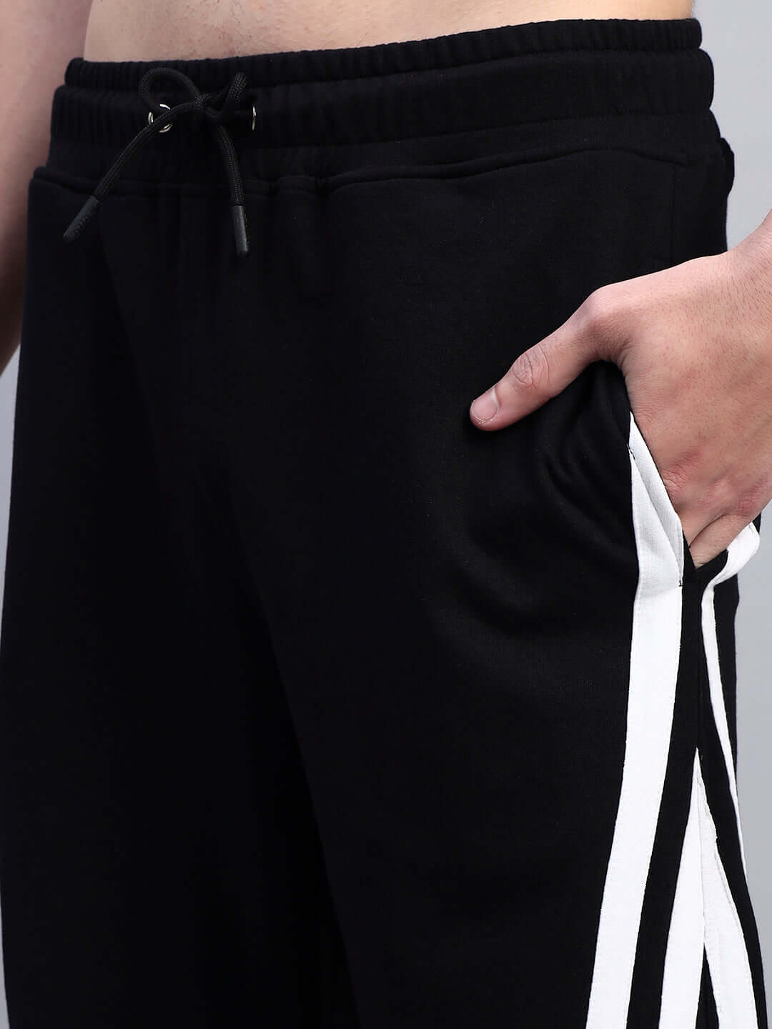 Close-up of black relaxed-fit joggers with multi-pocket design and white stripe detailing, worn by a model.