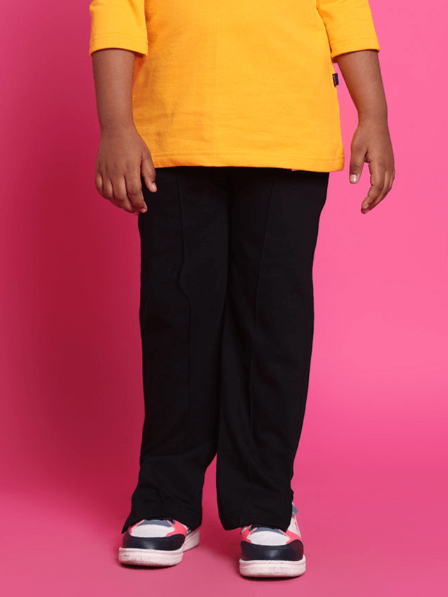 Child wearing black jogger pants with colorful sneakers standing against a pink background.