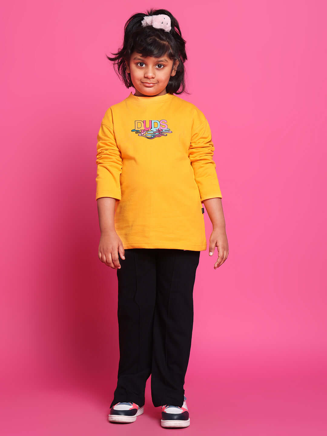 Child dressed in yellow-black CUBE CO-ORD outfit, made-to-order by DUDS, standing against a pink background.