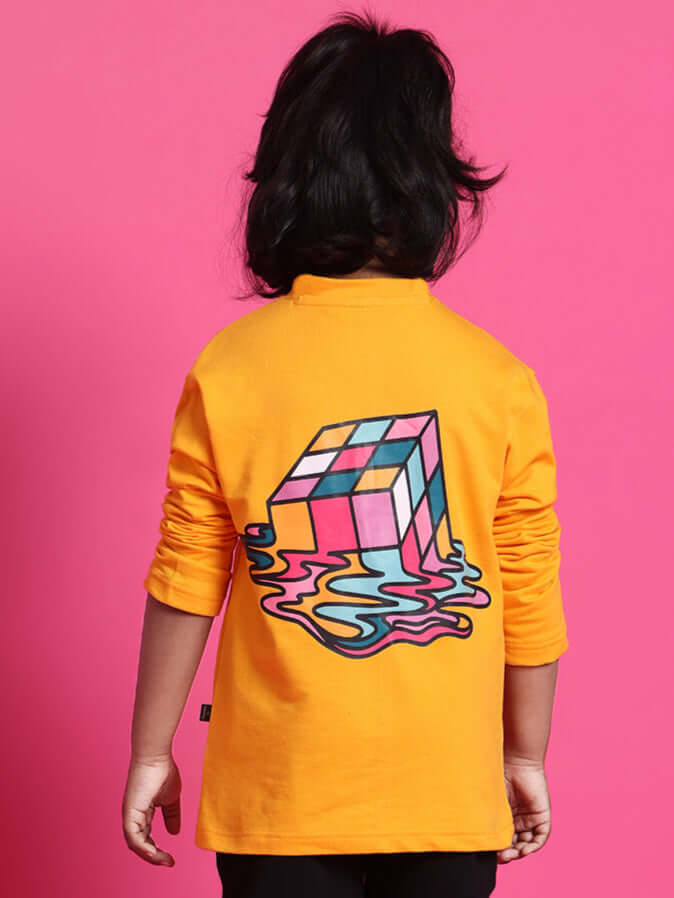 Child wearing a yellow oversized sweatshirt with a colorful cube design on the back, standing against a pink background.