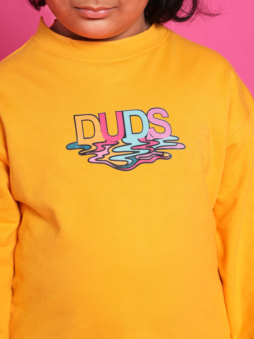 Child wearing yellow DUDS sweatshirt with colorful logo on front.