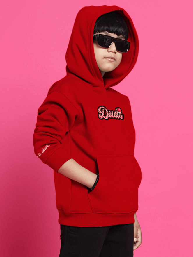 Child wearing a red oversized cupcake hoodie with embroidered text, against a pink background, suitable for boys and girls.