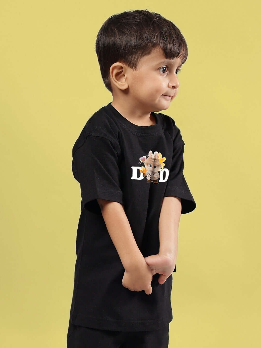 Young child wearing a black Cute Monsters T-shirt for boys and girls, featuring a whimsical cartoon design, against a yellow background.
