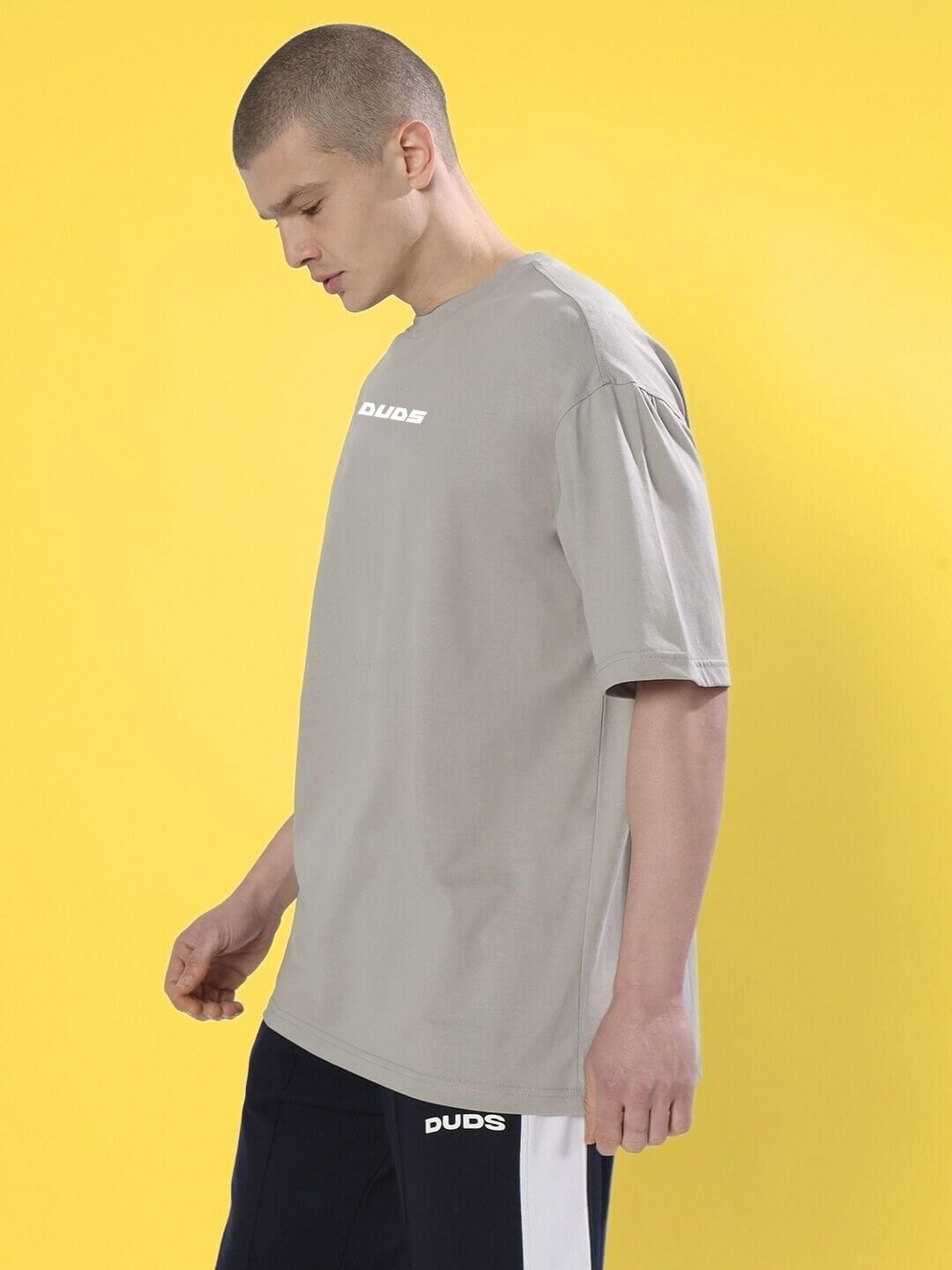 Model wearing CYBERPUNK OVER-SIZED T-SHIRT GREY against yellow background, showcasing urban streetwear style.