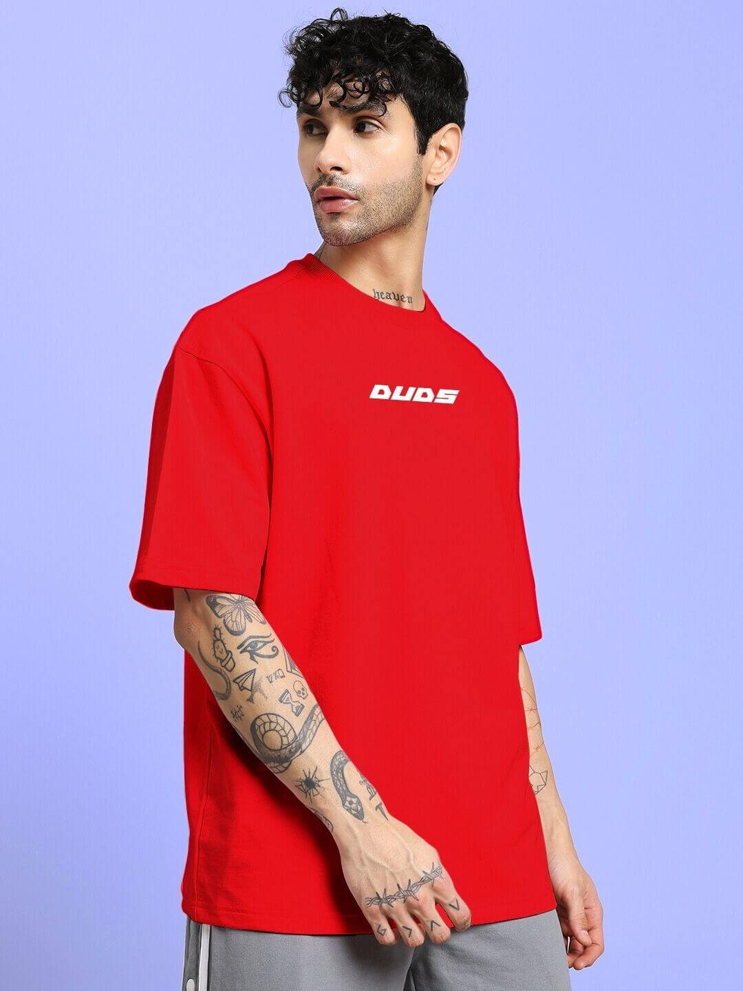 Man wearing CYBERPUNK OVER-SIZED T-SHIRT RED with bold street style and tattooed arm, standing against a blue background.