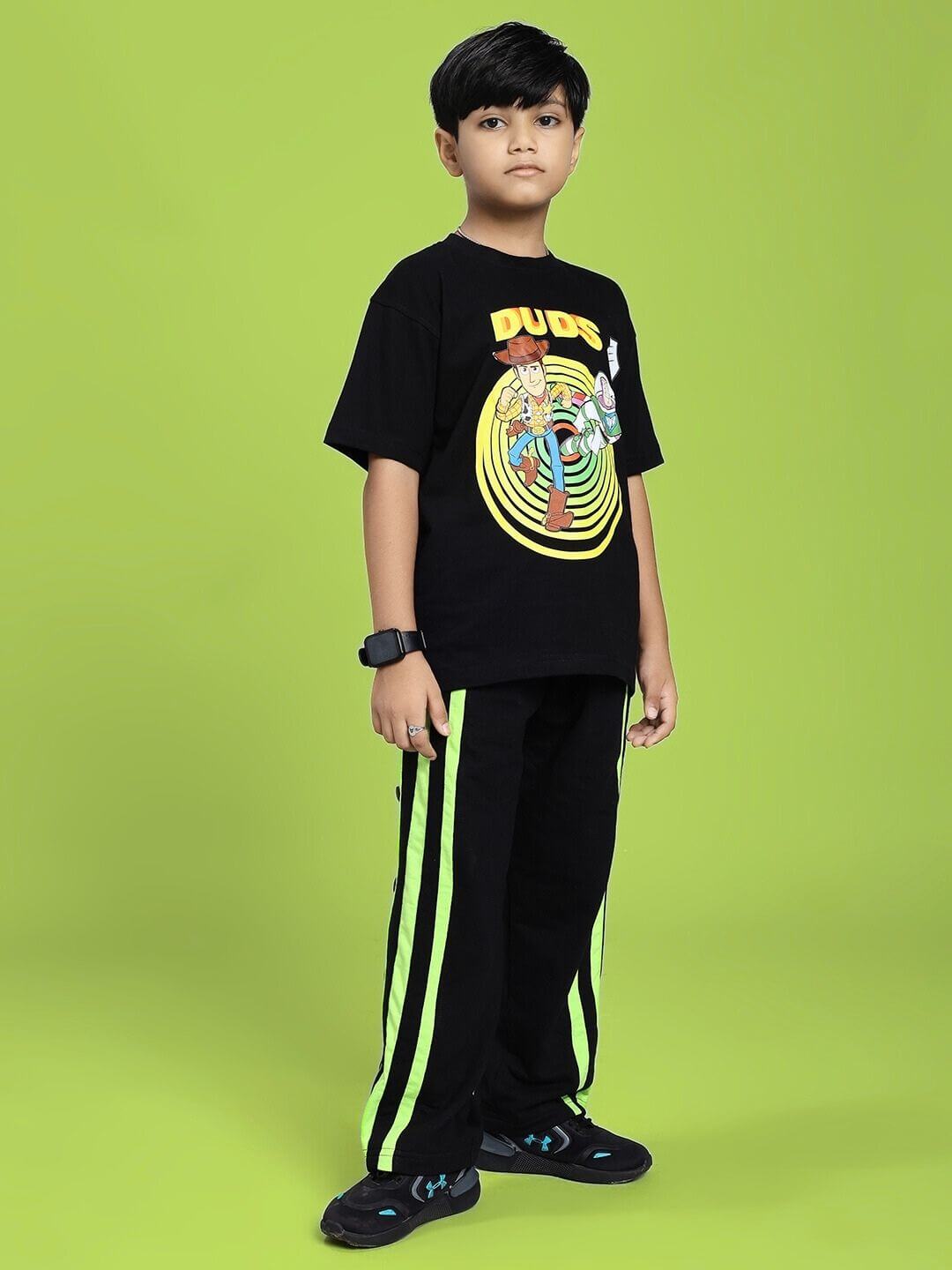 Child wearing DANCER JOGGER FOR BOYS AND GIRLS BLACK NEON-GREEN with graphic t-shirt, standing against green background.