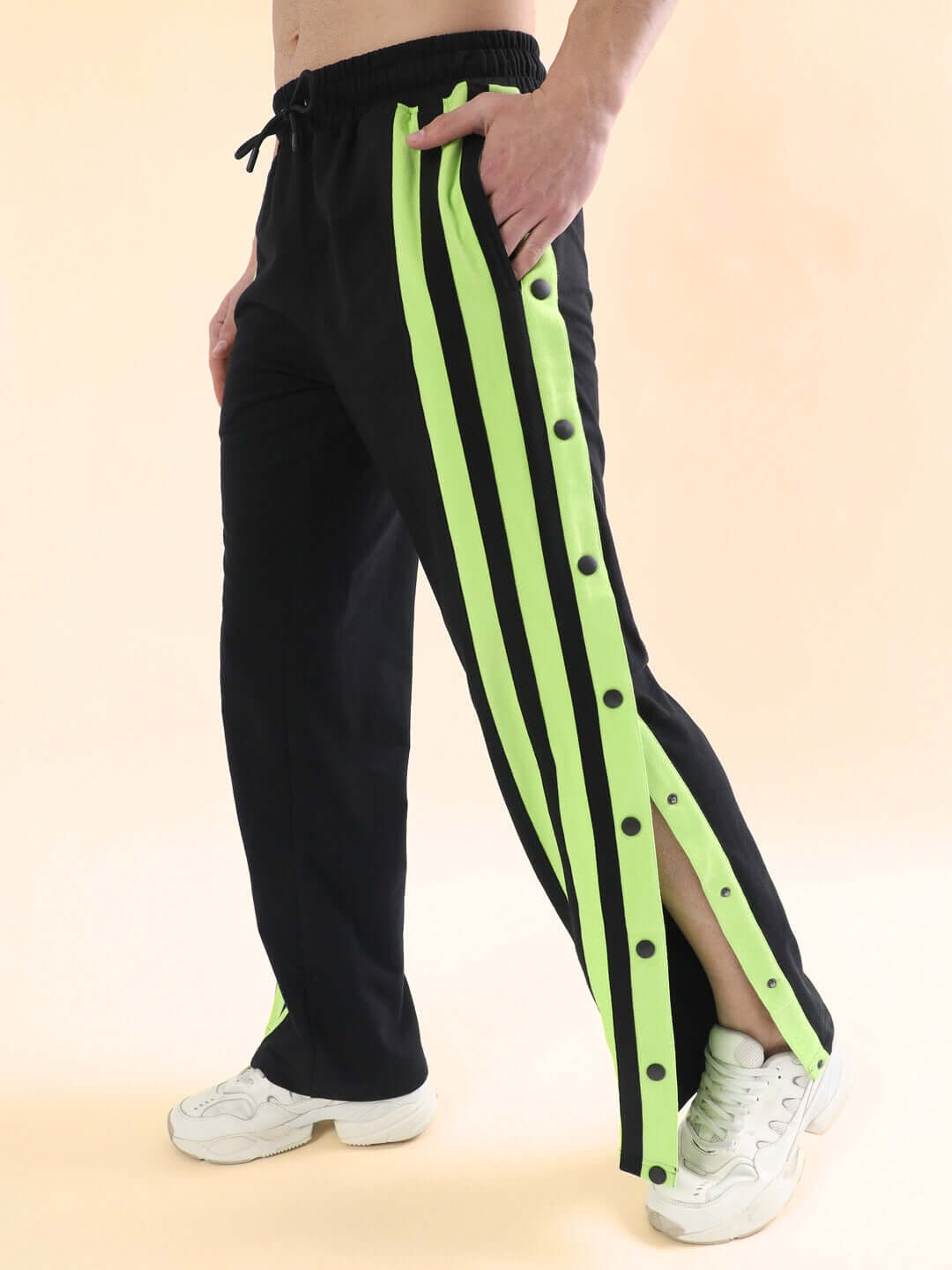 Person wearing black joggers with neon green stripes and buttons, styled for dance flexibility, paired with white sneakers.