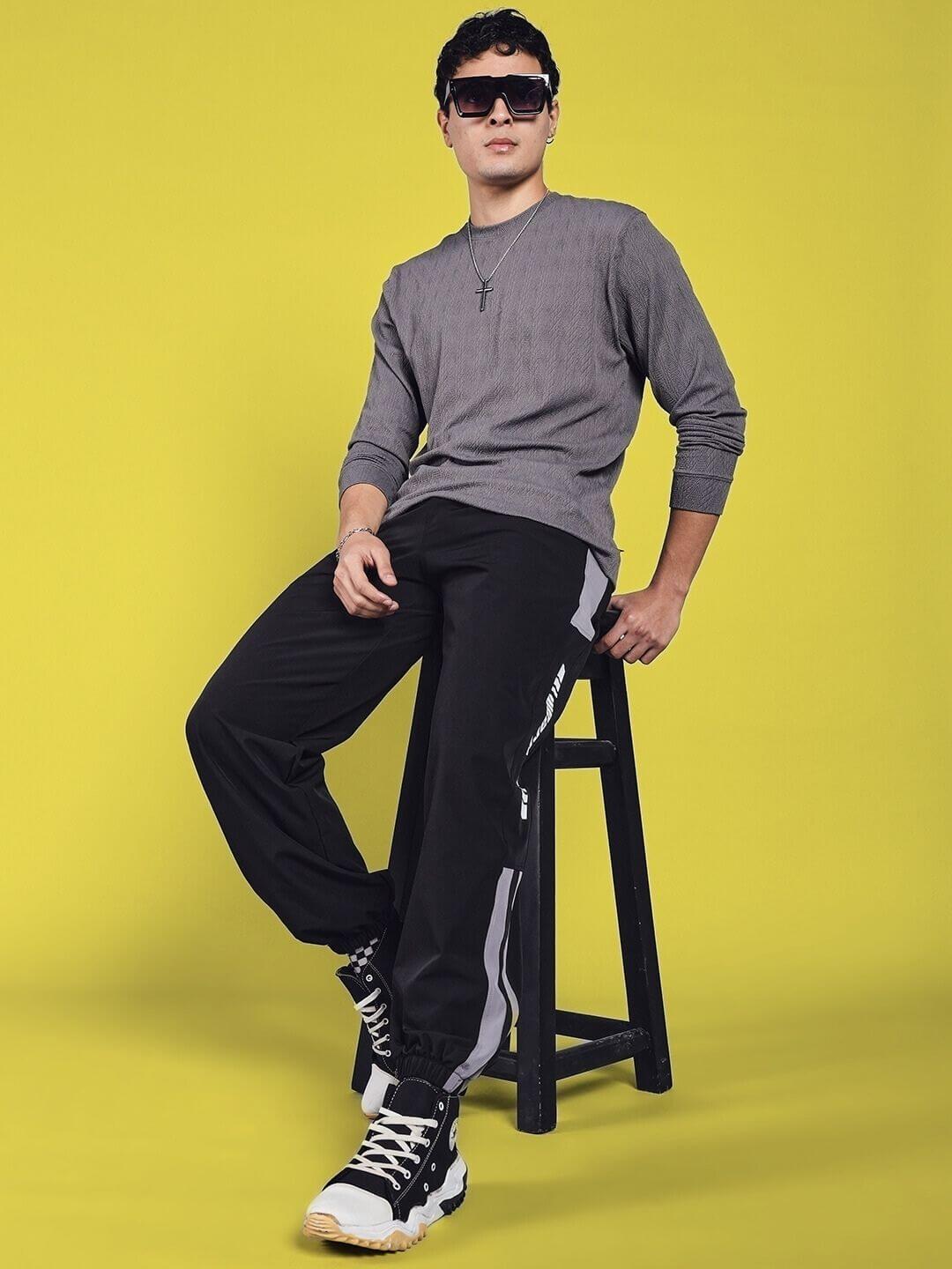 Model wearing Danny Relaxed Fit Cargo Pants in black, seated on a stool against a yellow background, showcasing casual style.