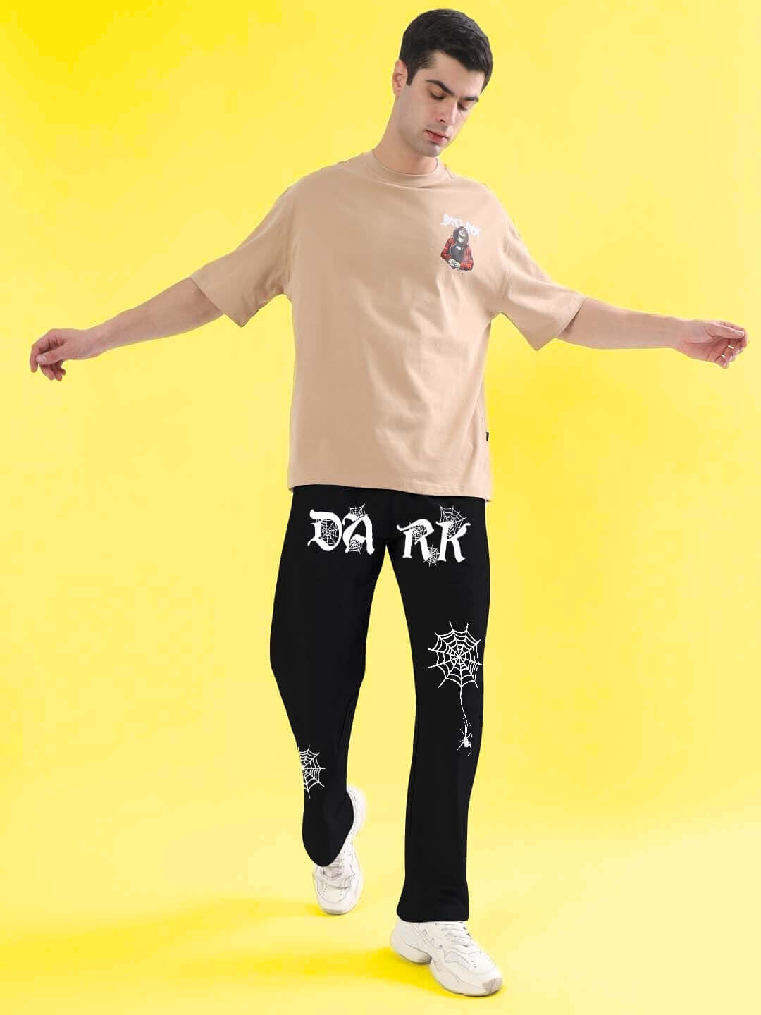Model wearing DUDS Dark Web Relaxed Jogger in black, featuring custom fit options and unique spider web graphics, on a yellow background.