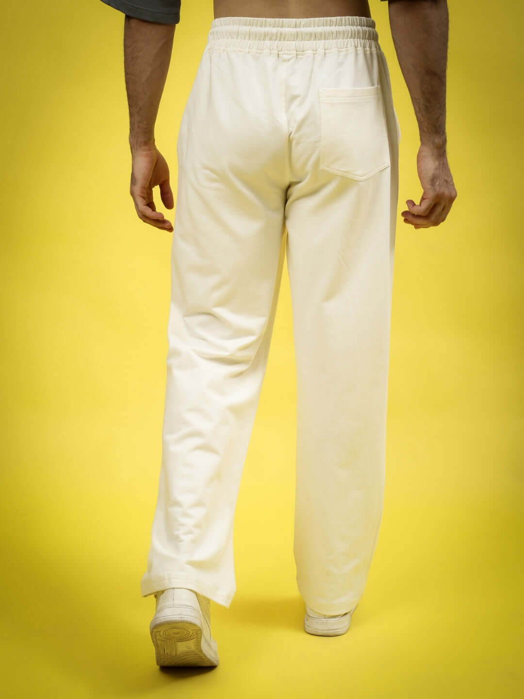Back view of off-white joggers with elastic waistband, styled for comfort and fashion, set against a yellow background.