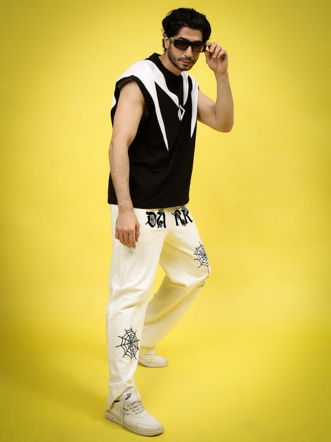 Man wearing Dark Web Relaxed Jogger in off-white with spider web design, paired with black sleeveless top and sunglasses.