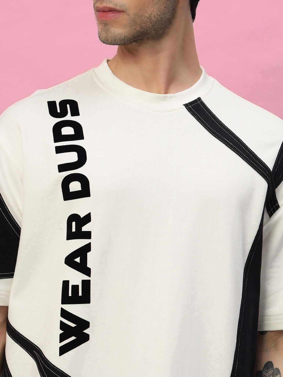 Model wearing DAVID DESIGNER OVERSIZED T-SHIRT OFF WHITE BLACK with bold text 'WEAR DUDS' and black detailing on a pink background.