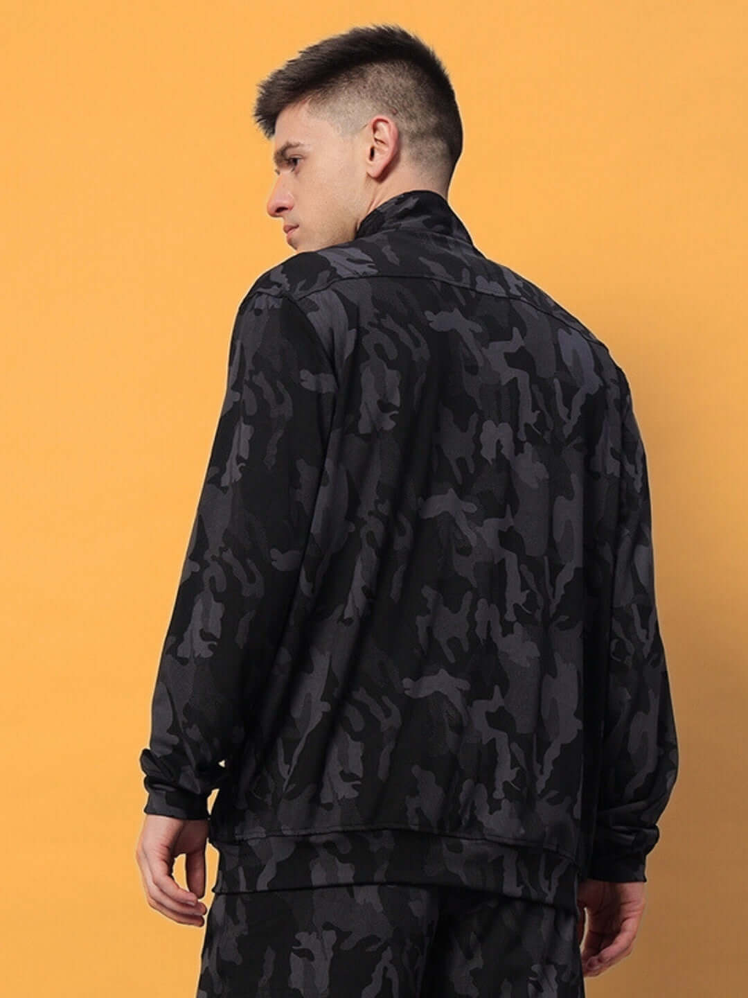 Back view of a man wearing a navy camo jacket against a yellow background.