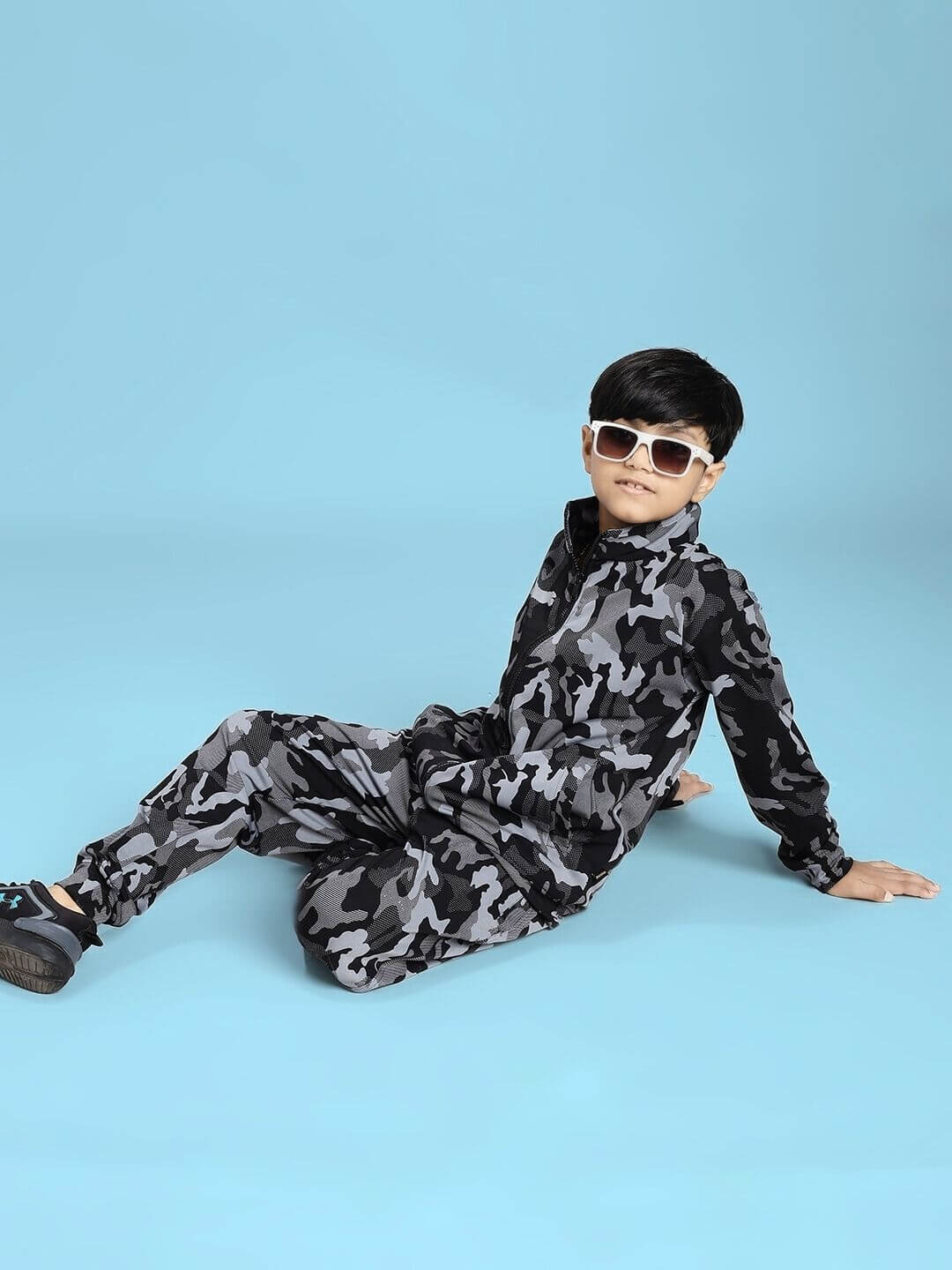 DEFENCE CAMOFLAUGE JACKET FOR BOYS AND GIRLS BLACK GREY worn by a child sitting on a blue background.