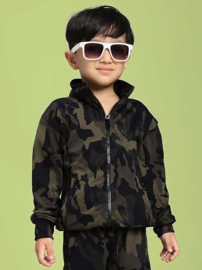 DEFENCE CAMOFLAUGE JACKET FOR BOYS AND GIRLS CAMO GREEN modeled by a child wearing sunglasses against a light green background.